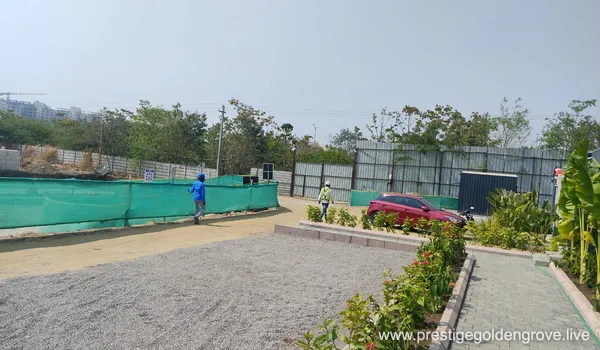 Landscaped site compound and entrance area at Prestige Golden Grove, Velimela, with safety fencing and distant towers under construction.