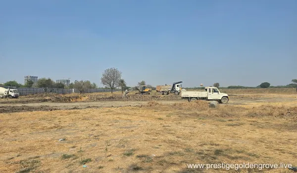 Early land-clearing and earthwork on the cleared plot at Prestige Golden Grove, Velimela, with an excavator, tipper truck and a pickup on site.